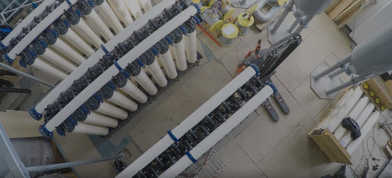 Large industrial water-treatment interior, with water-treatment elements and pipes; a sign reads "grey water"